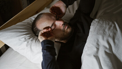 A hispanic man with a beard and no hair resting in a dark bedroom, portraying a serene late-night indoor atmosphere.