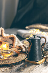 Cozy home composition with teapot, cup of tea, candles and a knitted element.