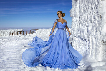 Beautiful elegant woman wearing blue fluttering long dress and is posing on a sunny day in the...