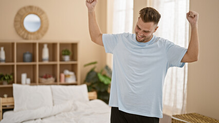 A cheerful man celebrates with raised fists in a cozy, well-decorated bedroom, exuding positive energy.