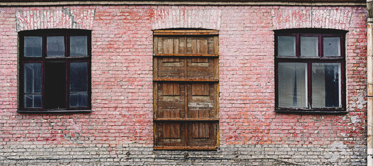 Front panoramic view of antique building facade with wooden door and windows mounted on shabby wall from red brick material