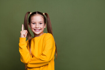 Portrait of smart clever small kid with tails dressed yellow sweatshirt raising finer up has idea isolated on khaki color background