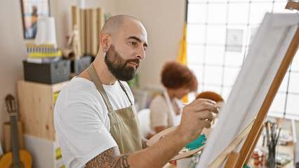 Two artists, a man and a woman, wear aprons in an indoor studio, concentrating on drawing together...