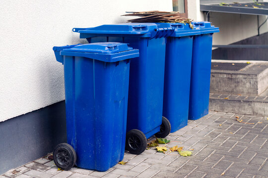Set of blue plastic trash bins for waste collection placed at urban street outside of building