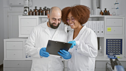 Fototapeta premium Two smiling scientists in the lab, engrossed in a lively chat while scrutinizing documents on clipboard