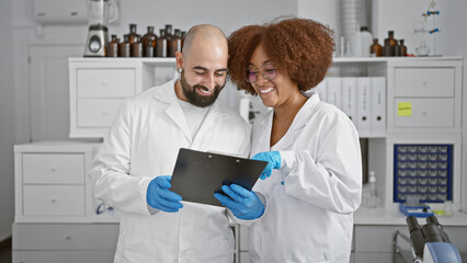 Two smiling scientists in the lab, engrossed in a lively chat while scrutinizing documents on...