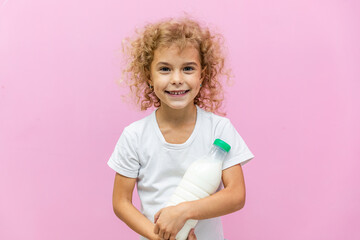 Little girl with a bottle of milk on a pink background