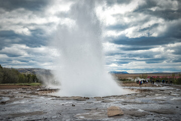 Famous Strokkur fountain geyser hot water eruption with cloudy sky and surrounding Icelandic...