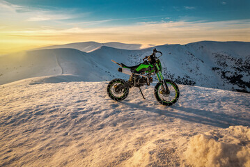 Extreme cross sport motorcycle in winter snowy mountains at sunset