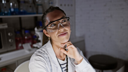 Young beautiful hispanic woman scientist doubting, playing with her glasses at the lab - a portrait of a serious professional, focused on her research under dim light