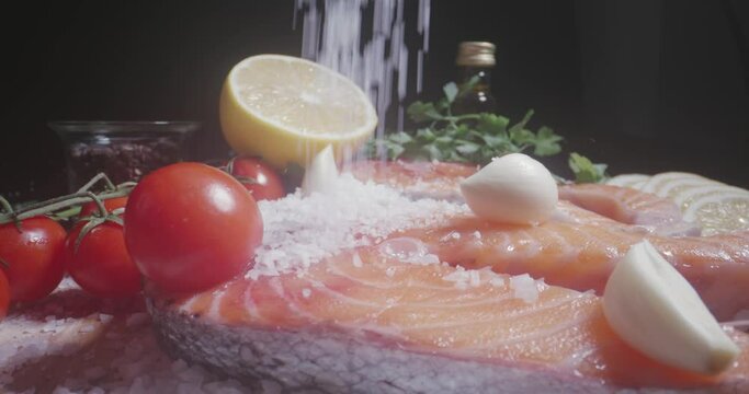 Pouring salt in slow motion on fresh fish steak fillets of raw salmon with lemon and spices, cinematic arrangement composition set