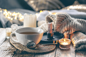 Cozy home composition with a cup of tea, candles and a knitted element.