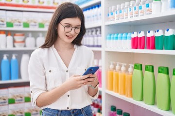 Young caucasian woman customer smiling confident using smartphone at pharmacy