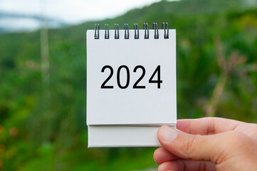 Hand holding 2024 white calendar with nature background. Holiday and calendar concept
