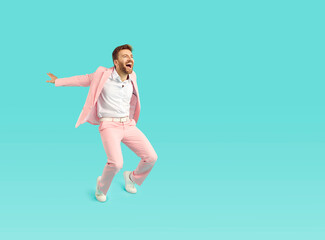 Happy funny man in stylish pink suit dancing on bright blue color copy space background looking at empty blank copyspace side, asking for attention, screaming, advertising sale, inviting to cool party