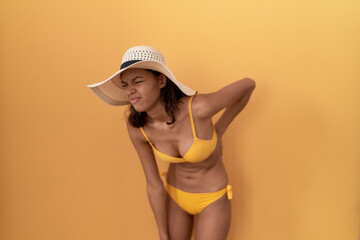 Young hispanic woman wearing bikini and summer hat suffering of backache, touching back with hand, muscular pain