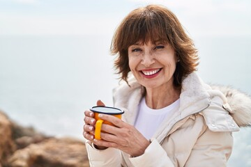 Middle age woman drinking coffee sitting on the rock at seaside © Krakenimages.com