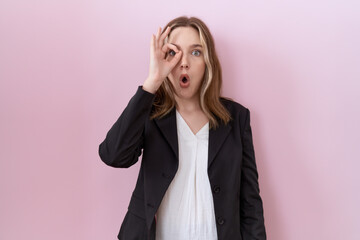 Young caucasian business woman wearing black jacket doing ok gesture shocked with surprised face, eye looking through fingers. unbelieving expression.