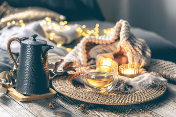 Cozy home composition with teapot, cup of tea, candles and a knitted element.