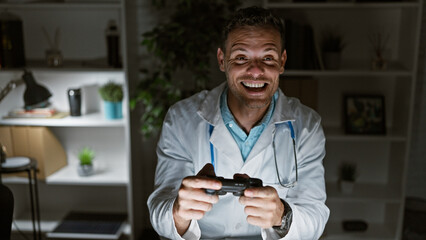 A cheerful young hispanic man in a lab coat joyfully plays video games in a modern indoor office setting. © Krakenimages.com
