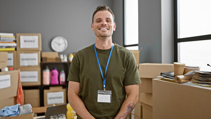 Hispanic man with beard smiling in warehouse interior wearing lanyard amongst boxes