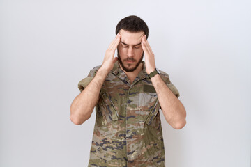 Young hispanic man wearing camouflage army uniform with hand on head for pain in head because...