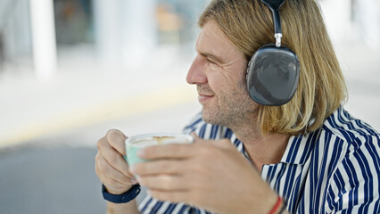 A smiling man wearing headphones enjoys coffee outdoors at a modern urban cafe.
