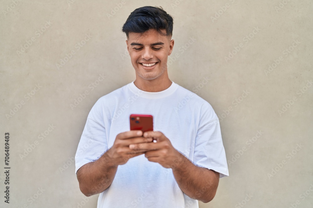 Sticker Young hispanic man smiling confident using smartphone over isolated white background