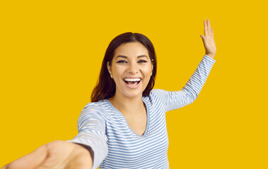 Cheerful funny woman who reaches out to camera to have fun and dance with you on yellow background....