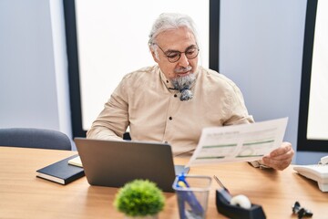 Middle age grey-haired man business worker using laptop reading document at office