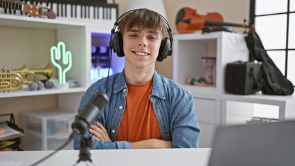 Smiling teenage boy in headphones sits in a music-themed room with a microphone and guitar.