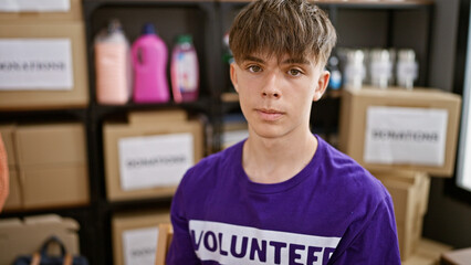 Caucasian male teenager volunteering at an indoor donation center, standing confidently amid...