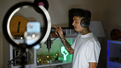 Smiling young latin man, a tattooed musician, singing his heart out and dancing in a dimly lit music studio while recording a catchy song for a video