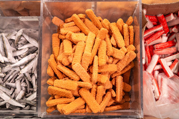 Frozen breaded orange fish fingers sticks in the market fridge as a background.