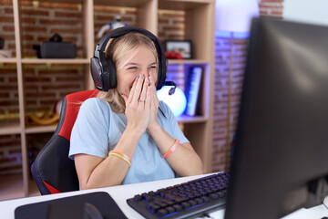 Young caucasian woman playing video games wearing headphones laughing and embarrassed giggle...