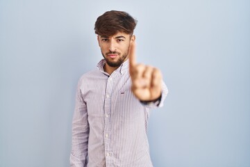 Arab man with beard standing over blue background pointing with finger up and angry expression, showing no gesture