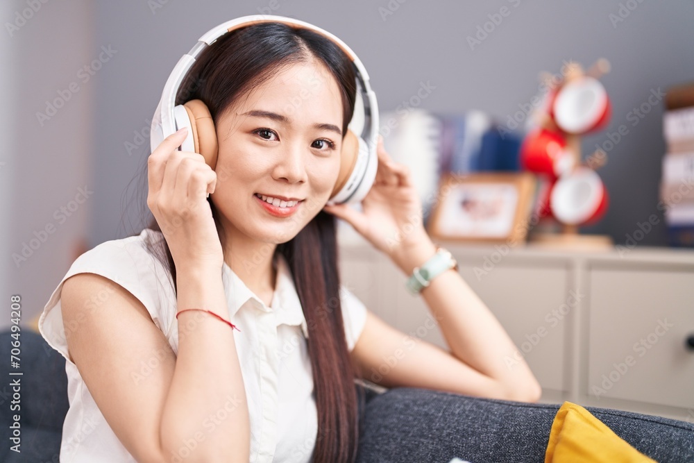 Wall mural young chinese woman listening to music sitting on sofa at home