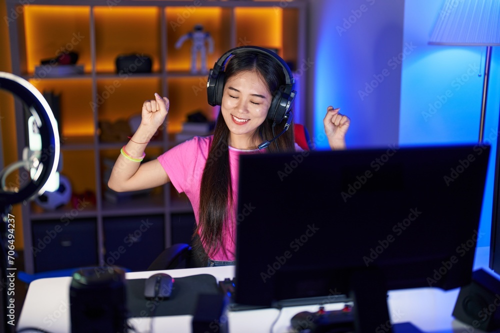 Sticker Young chinese woman streamer playing video game with winner expression at gaming room