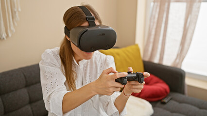 Young caucasian woman enjoying virtual reality headset at home, sitting on gray couch holding game controller.