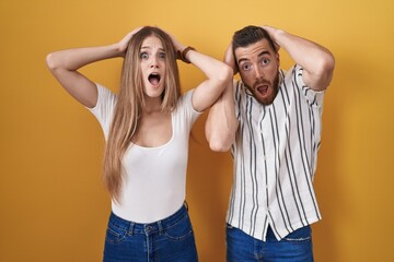 Young couple standing over yellow background crazy and scared with hands on head, afraid and surprised of shock with open mouth