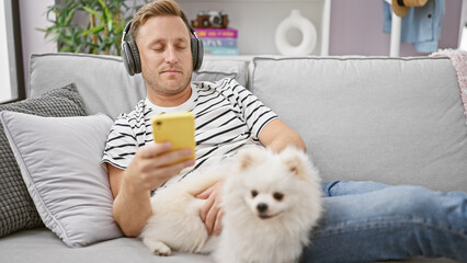 At home, a young man, casually engrossed in the digital world, sits back relaxed on the sofa with...