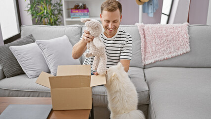 Confident young caucasian man happily unpacking a surprise teddy bear from a cardboard box at home,...