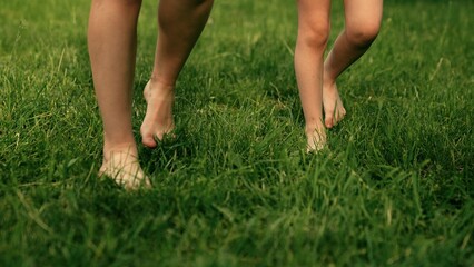 Barefoot mom, boy, girl go on green grass in park. Bare feet mom, child, close-up go on green...