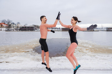 Young couple jumping and giving hi five after winter sauna. Cold exposure for better health and mood. Swim in ice cold water. Practice to boost immunity. Nordic lifestyle with the urban background