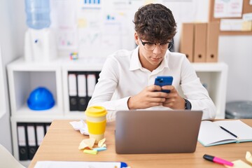 Young hispanic teenager business worker using laptop and smartphone at office