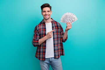 Photo of funky good mood man dressed plaid shirt pointing finger cash fan isolated turquoise blue...