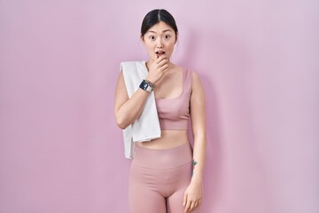 Chinese young woman wearing sportswear and towel looking fascinated with disbelief, surprise and amazed expression with hands on chin