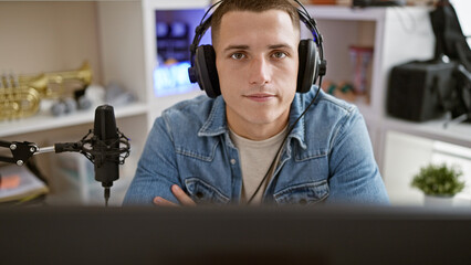 Handsome young hispanic man podcasting with microphone and headphones in a studio setting.