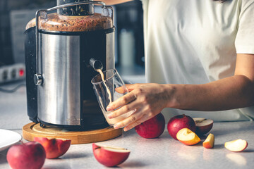 A woman makes apple juice at home with a juicer.
