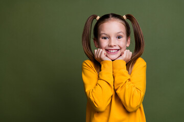 Photo of cute lovely overjoyed schoolgirl with ponytails wear yellow pullover hold hands under chin isolated on khaki color background